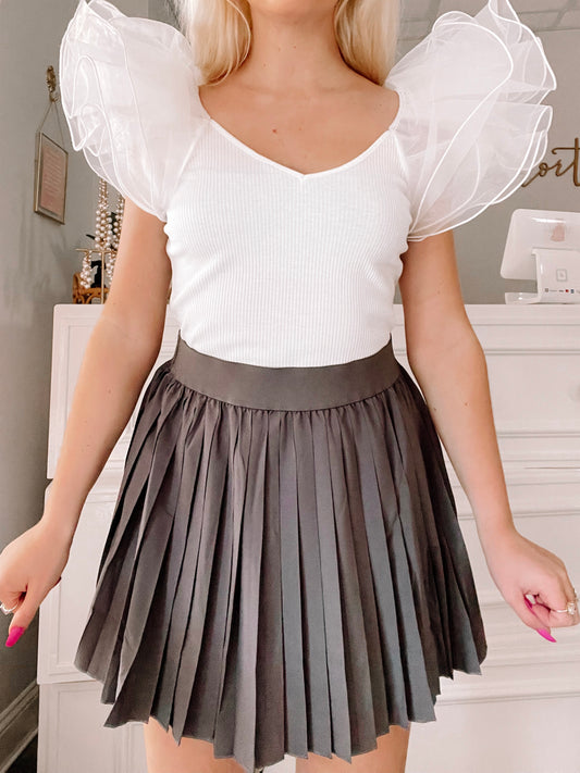 Dark gray pleated mini skirt styled with a white ribbed top, shown on a model.
