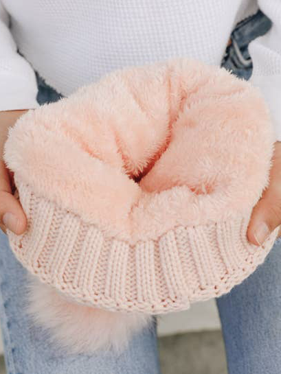 Soft pink beanie with fluffy lining, shown being held.

