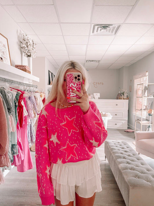Hot pink star-print sweater styled with white ruffle shorts in a boutique setting.